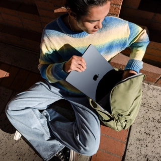 Вид спереди человека, кладущего закрытый 15-дюймовый MacBook Air в сумку.