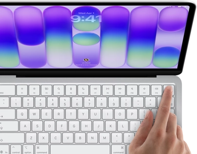 MacBook Neo, silver color, showing login screen, person's finger on Touch ID sensor in top-right corner of keyboard
