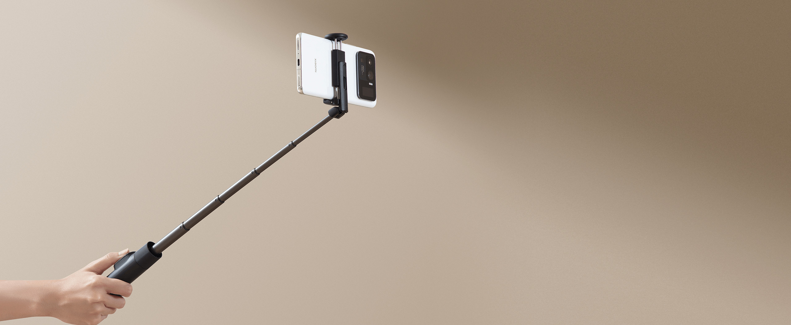 Разгънат Xiaomi Selfie Stick Tripod Mini, държан в ръка със смартфон в щипката