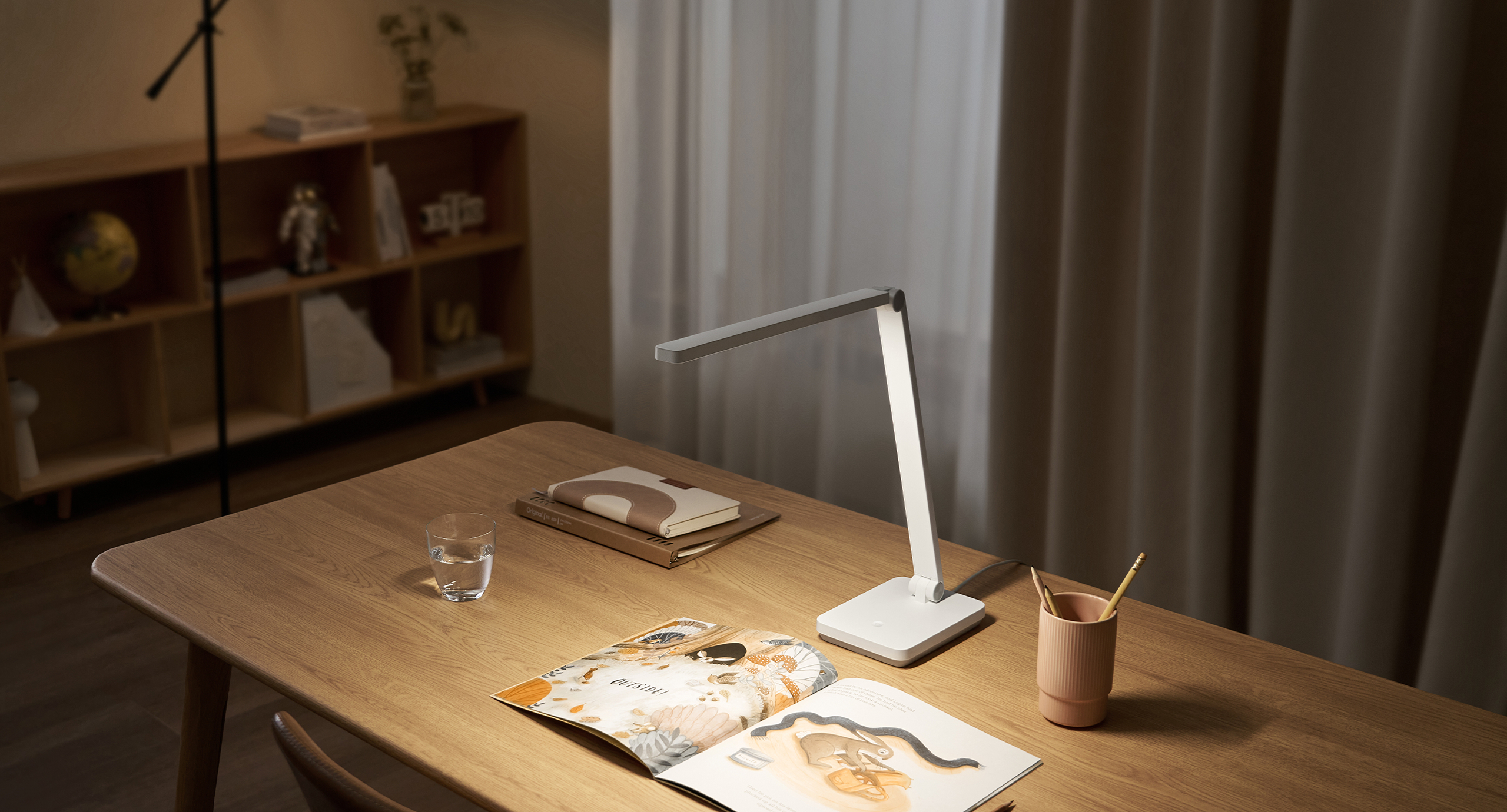 Настолна лампа Xiaomi Desk Lamp Lite, включена върху дървено бюро с разтворена книга вечер