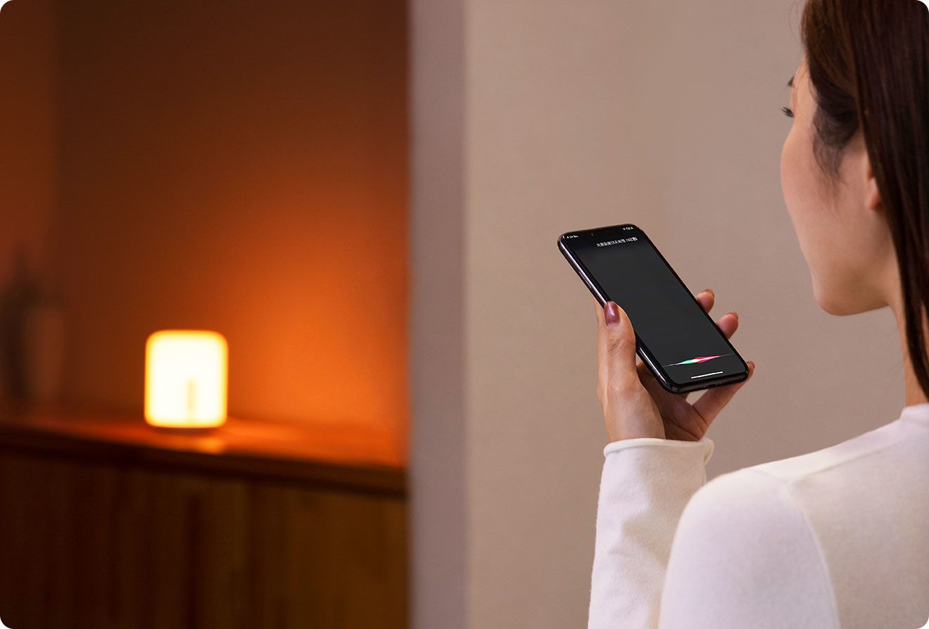 Жена дава гласова команда на смартфон, а Mi Bedside Lamp 2 свети в топло жълто