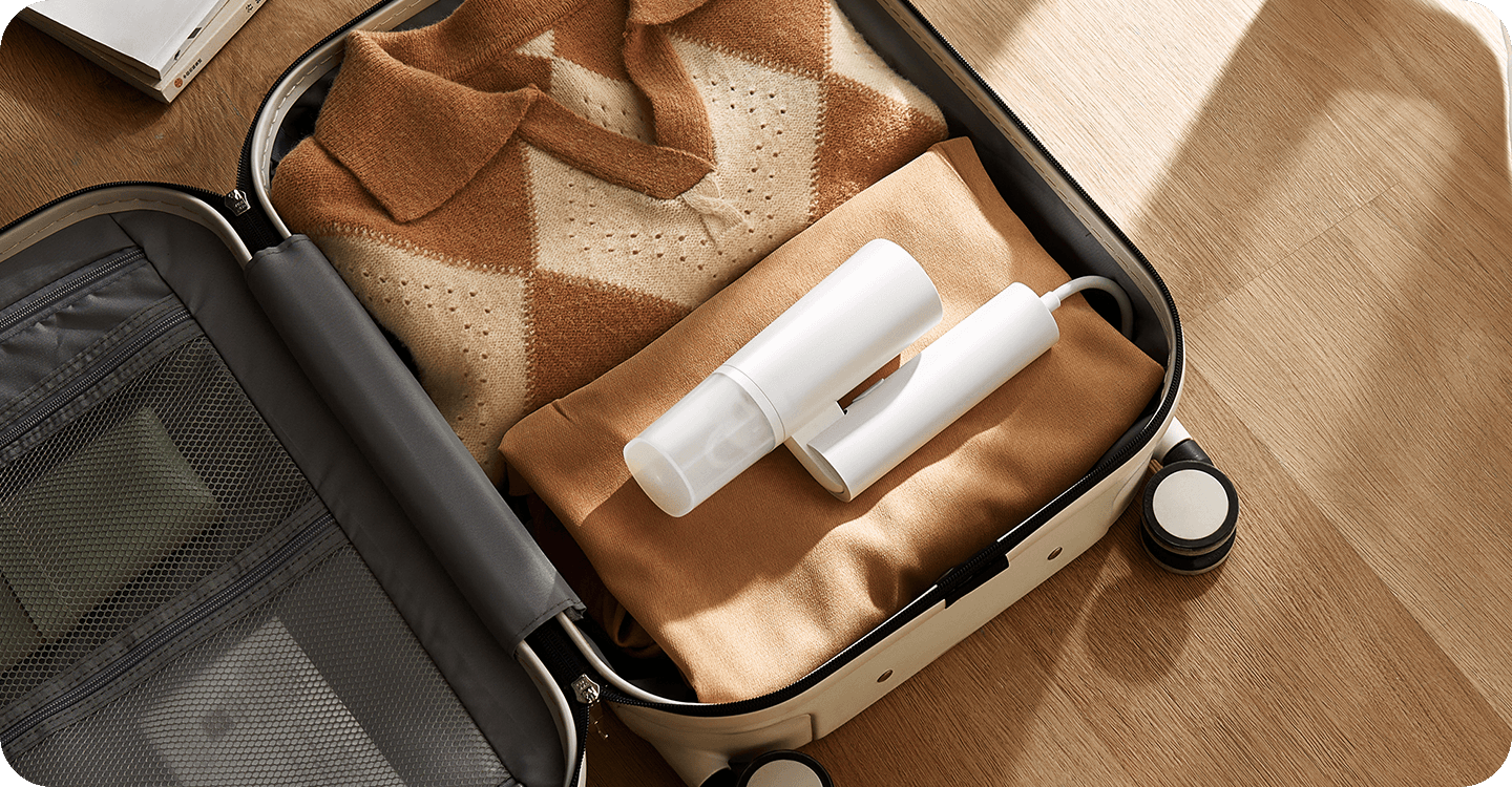 Сгънатият Xiaomi Handheld Garment Steamer, прибран в куфар с дрехи