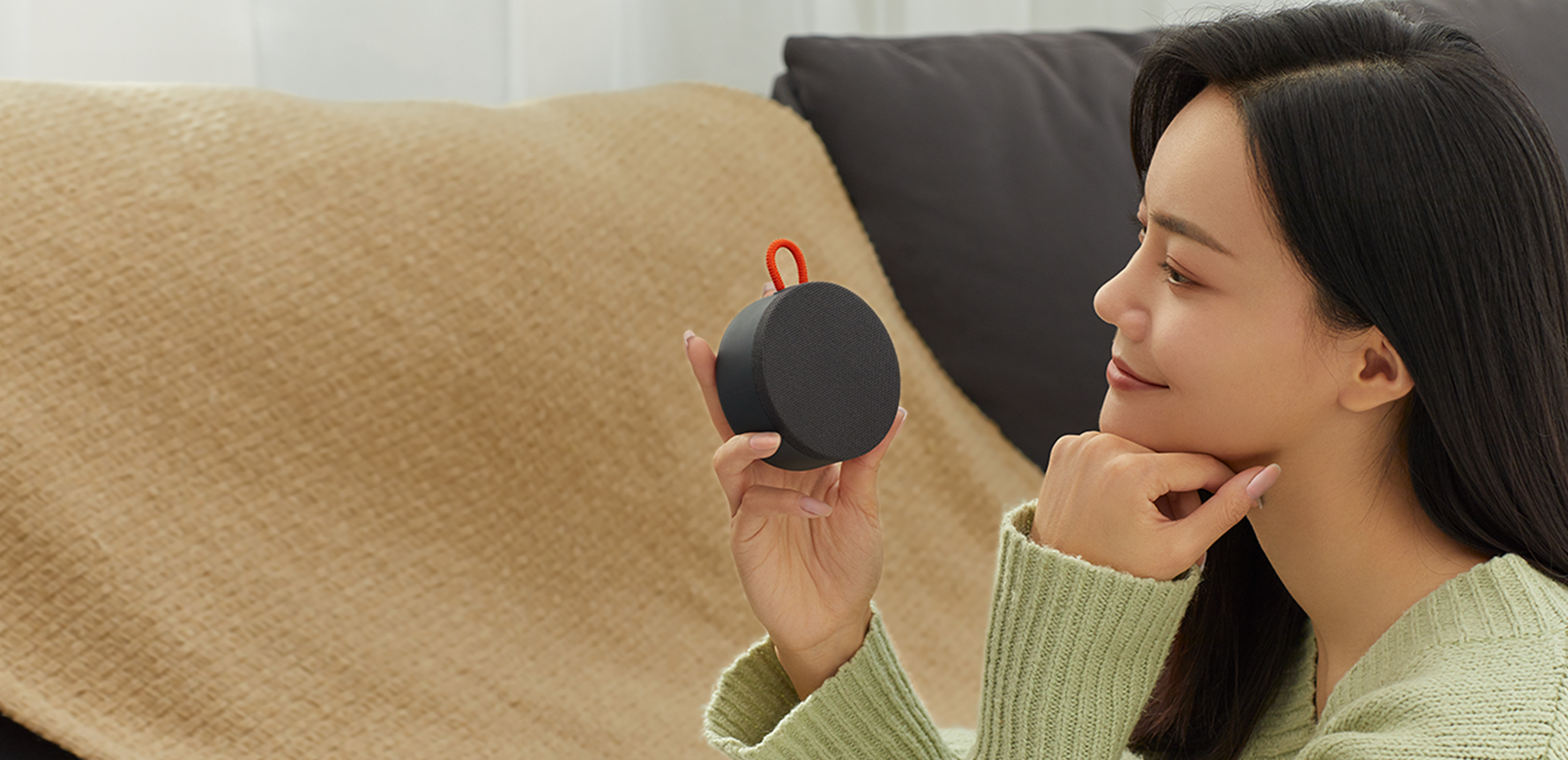 Жена държи Mi Portable Bluetooth Speaker в ръка, докато води разговор на дивана