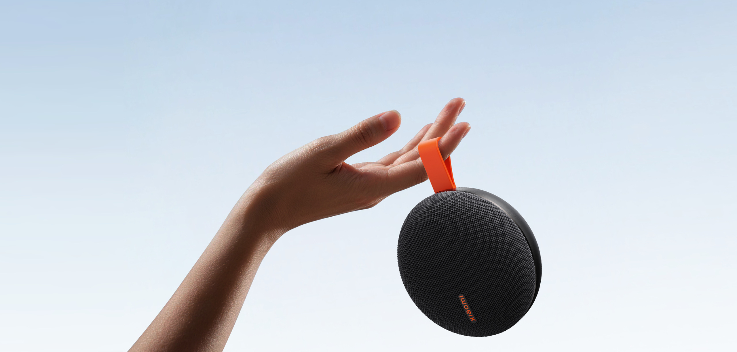 Черна колонка Xiaomi Bluetooth Speaker Essential с оранжева каишка на фона на небе